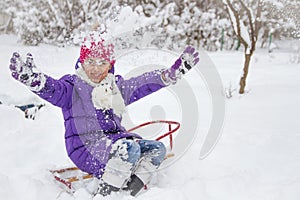 Child girl in park on sledge playing with snow