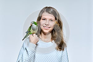 Child girl with pet green quaker parrot looking at camera on light studio background