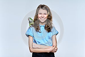 Child girl with pet green quaker parrot looking at camera on light studio background