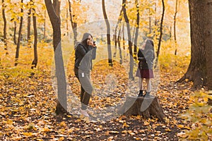 Mother photographer takes pictures of a her daughter in the park in autumn. Hobbies, photo art and leisure concept.