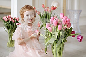Child girl in a pink dress among tulips in vases