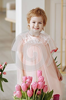 Child girl in a pink dress among tulips in vases