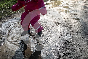 Child / girl with pink rainwear jumping water pool / puddle