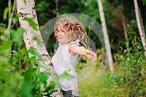 Child girl playing with birch tree in summer forest