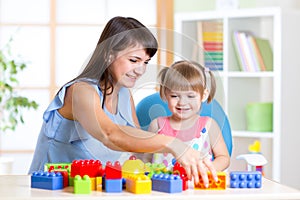 Child girl playing construction set with mother