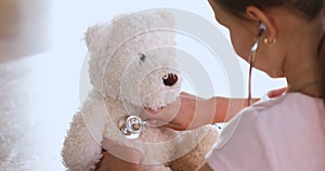 Child girl playing doctor holding stethoscope listening teddy bear, closeup
