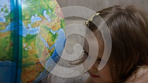 Child girl playing with globe. Baby studies geography and a map of the world.