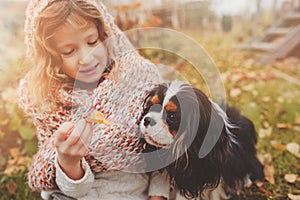 Child girl playing with her dog in autumn garden on the walk