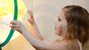 Child girl playing with an illuminated globe. Baby studies geography and a map of the world