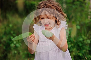 Child girl playing with leaves in summer forest with birch trees. Nature exploration with kids.