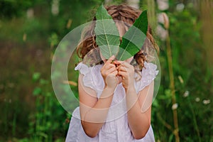 Child girl playing with leaves in summer forest with birch trees. Nature exploration with kids.