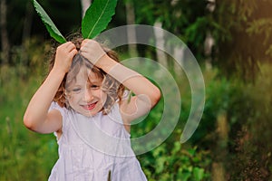 Child girl playing with leaves in summer forest with birch trees. Nature exploration with kids.