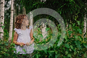 Child girl playing with leaves in summer forest with birch trees. Nature exploration with kids.