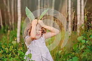 Child girl playing with leaves in summer forest with birch trees. Nature exploration with kids.