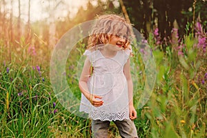 Child girl playing with leaves in summer forest. Nature exploration with kids