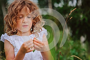 Child girl playing with leaves in summer forest. Nature exploration with kids