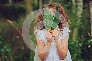 Child girl playing with leaves in summer forest. Nature exploration with kids