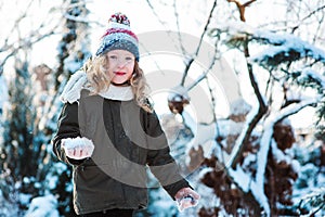 Child girl playing with snow in winter garden or forest, making snowballs and blowing snowflakes