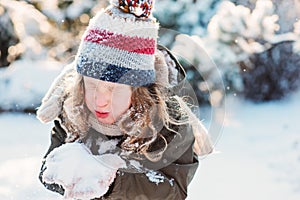 Child girl playing with snow in winter garden or forest, making snowballs and blowing snowflakes