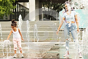 Child girl playing with water in the fountain with mom, family relationships, summer, walk in the park
