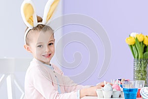 Child girl playing wearing bunny ears by table with Easter photo