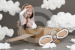 The child girl plays in an airplane made of cardboard box and dreams of becoming a pilot, clouds of cotton wool on a gray backgrou