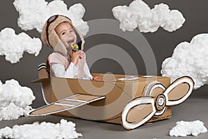 The child girl plays in an airplane made of cardboard box and dreams of becoming a pilot, clouds of cotton wool on a gray backgrou