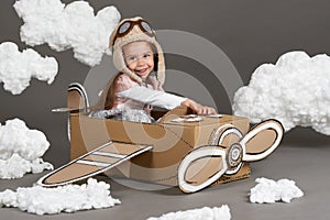 The child girl plays in an airplane made of cardboard box and dreams of becoming a pilot, clouds of cotton wool on a gray backgrou