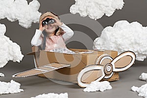 The child girl plays in an airplane made of cardboard box and dreams of becoming a pilot, clouds of cotton wool on a gray backgrou