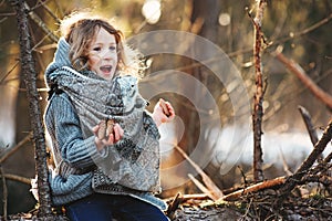 Child girl plays with pine cones on tree log in winter forest