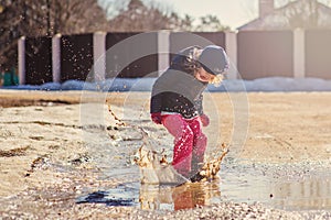 Child girl plays puddle jumping in early spring