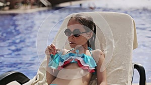 Child girl in the pool with a cocktail on a sun lounger