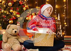 Child girl posing in new year or christmas decoration, wearing a red sweater and a Santa hat, she opens a gift box. She is