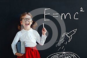 Child girl prodigy student with book near blackboard