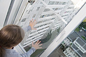 Child girl, pushes the mosquito net out of the window, a dangerous situation, on the background of the house, top view