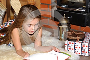 Child girl is reading in front of fireplace