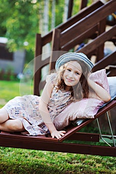 Child girl relaxing on sun bed in sunny garden, enjoying summer vacations