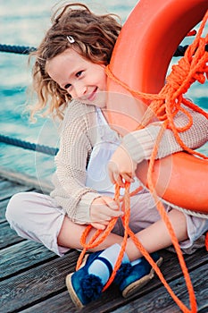 Child girl with rescue ring on wooden pier with sea background