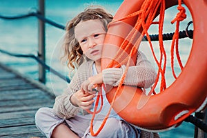 Child girl with rescue ring on wooden pier with sea background