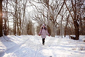 Child girl runs along the road in a snowy forest. Winter games for children. Outdoor entertainment concept.