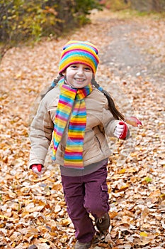 Child girl runs on a footpath in autumn forest through fallen leaves background