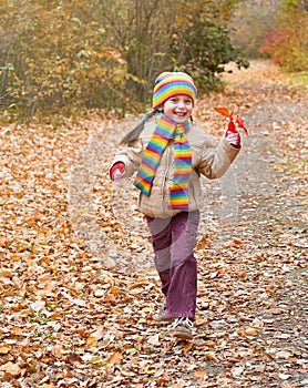 Child girl runs on a footpath in forest, autumn leaves background, fall season