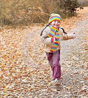 Child girl runs on a path in forest, autumn leaves background, fall season