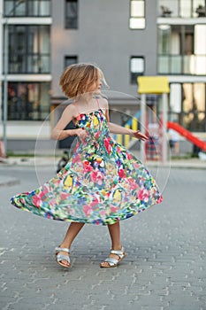Child girl runs, spins, spins and dances on street in summer. Childhood and vacation concept