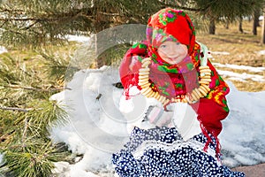 Child girl in Russian pavloposadskie folk scarf on head with floral print and with bunch of bagels on background of snow.