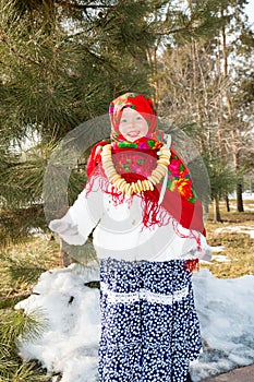 Child girl in Russian pavloposadskie folk scarf on head with floral print and with bunch of bagels on background of snow.