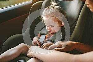 Child girl in safety car seat and mother fastens belt family road trip lifestyle