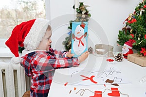 Child girl in Santa hat making christmas greeting card with snowman