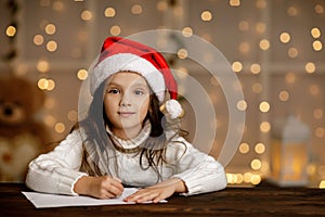 Child girl in santa hat writing letter to Santa Claus