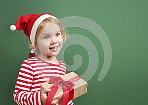 Child girl in santa red hat with box on green empty space background.Kid with christmas gift